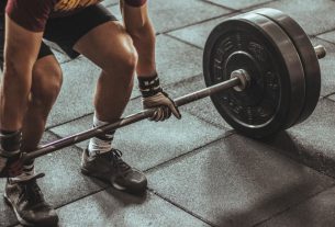A focused weightlifter prepares to lift a heavy barbell in an indoor gym setting.
