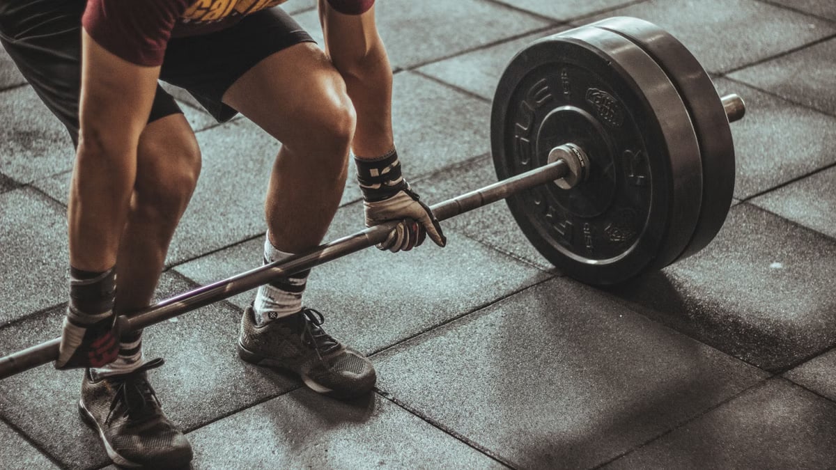 A focused weightlifter prepares to lift a heavy barbell in an indoor gym setting.